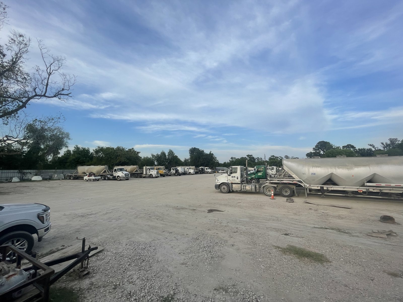 Wide view of the open caliche apron at the Eazy Trans Houston yard, with trucks parked along the far tree line